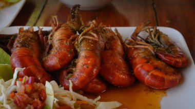 Fotoğrafta soslu iki dev karides tabağı var. Ayrıca parlak bir tabakta lahana salatası ve domates var. Sıcak yemekli yemekler elmas şeklinde düzenlenir. Üst görünüm.
