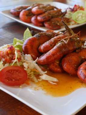 Fotoğrafta soslu iki dev karides tabağı var. Ayrıca parlak bir tabakta lahana salatası ve domates var. Sıcak yemekli yemekler elmas şeklinde dizilir..