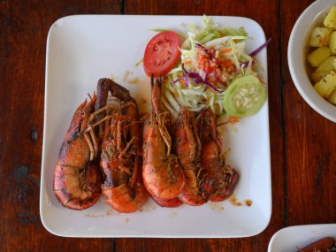 Fotoğrafta soslu iki dev karides tabağı var. Ayrıca parlak bir tabakta lahana salatası ve domates var. Sıcak yemekli yemekler elmas şeklinde düzenlenir. Üst görünüm.