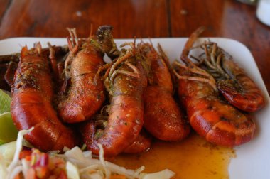Fotoğrafta soslu iki dev karides tabağı var. Ayrıca parlak bir tabakta lahana salatası ve domates var. Sıcak yemekli yemekler elmas şeklinde düzenlenir. Üst görünüm.