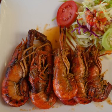 Fotoğrafta soslu iki dev karides tabağı var. Ayrıca parlak bir tabakta lahana salatası ve domates var. Sıcak yemekli yemekler elmas şeklinde düzenlenir. Üst görünüm.