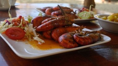 Fotoğrafta soslu iki dev karides tabağı var. Ayrıca parlak bir tabakta lahana salatası ve domates var. Sıcak yemekli yemekler elmas şeklinde düzenlenir. Üst görünüm.