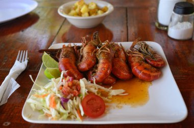 Fotoğrafta soslu iki dev karides tabağı var. Ayrıca parlak bir tabakta lahana salatası ve domates var. Sıcak yemekli yemekler elmas şeklinde dizilir..