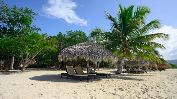 Cana umbrella on white beach. Sun lounger. Cana construction on hispaniola lagoon. Tourist trap in dominican resort for get a suntan. Tropical hideaway with palm tree and perfect white sand.