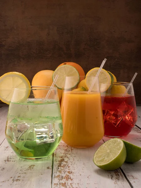 Fotoğrafta mango, limon, limon ve portakal gibi taze meyveler gösteriliyor. Foto 'nun merkezinde, içinde limon olan bir bardakta beyaz tahta masanın üzerinde üç mocktail var. Çilekli kokteyl, limonlu kokteyl..