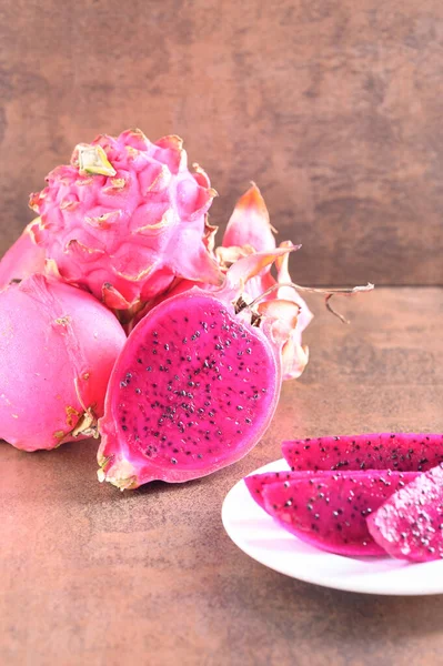 Photo shows vegan eating like pitahaya fruit of cactus. Pink color background. Organic exotic fruit on brown pattern.