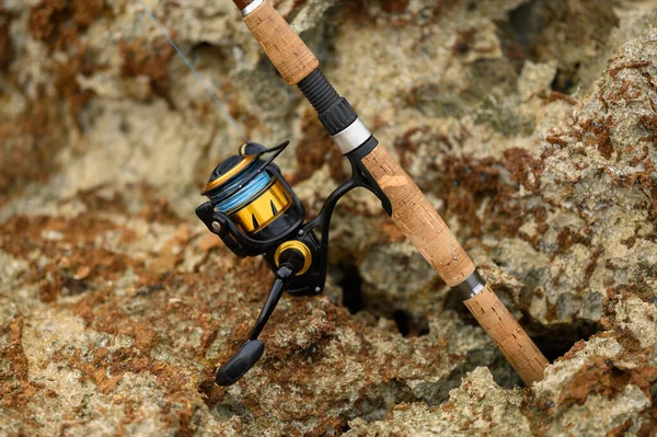 图为一个用于海洋捕捞的纺鱼竿 钓竿上的钓丝是可以看见的 钓竿的背景是海边的岩石 — 图库照片