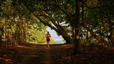 Fotoğraf orman ıslah bölgesindeki bir orman yolunu gösteriyor. Yumuşak kum kaplı doğal kaynaklı koşu bandı. Yeşil orman manzarası yürüyüş yolunun kahverengi kumuyla çelişiyor. Koşan adam..