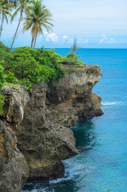 Fotoğraf Karayip Denizi 'ndeki dik bir uçurumu gösteriyor. Okyanus suyu berrak ve mavi. Mükemmel eğitimli mağara. Yeşil bitkiler kayalarda yetişir. Güzel bir deniz manzarası açılıyor.