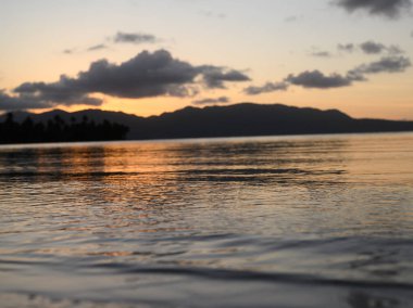 Fotoğraf, Atlantik Okyanusu 'nun arka planına karşı dağlarda gün doğumunu gösteriyor. Güneş dağın arkasında batar ve bulutlarda saklanır. Okyanus suyu yükselen güneşin parıltısını yansıtır..