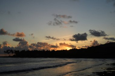 Fotoğraf, Atlantik Okyanusu 'nun arka planına karşı dağlarda gün doğumunu gösteriyor. Güneş dağın arkasında batar ve bulutlarda saklanır. Okyanus suyu yükselen güneşin parıltısını yansıtır..