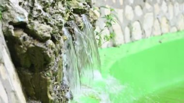Çeşme ve akan su yakında. Doğal gölde nehir taşları arasında akan su. Çeşmeli küçük bir gölet. Kristal su kaynağı ve damlalar güneş ışınlarını yansıtır. Saf su hareketi. Park ve göl.