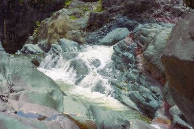 Fotoğraf dağ nehrinin aktığı kayalık bir vadi gösteriyor. Nehir büyük taş blokların arasından akar. Karayip adasının büyüleyici yaban hayatı orjinalliğiyle hayrete düşürüyor. Dağ nehrinin üst manzarası.