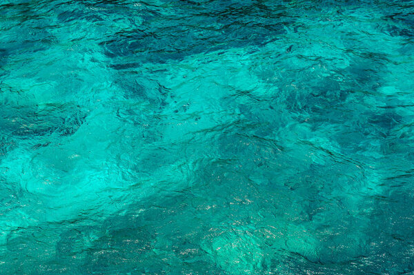 Photo shows texture of ocean. Surface of sea is turquoise. Ocean water pattern is light and in different shades of blue. Background of sea water is transparent and clean.
