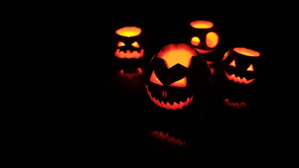 Muitas abóboras diferentes do Jack da cabeça do Halloween com sorriso assustador e velas ardentes para dentro para a noite da festa no fundo preto — Fotografia de Stock