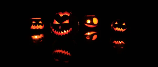 Veel verschillende Halloween hoofd Jack pompoenen met griezelige glimlach en brandende kaarsen binnen voor Party Night op zwarte achtergrond — Stockfoto