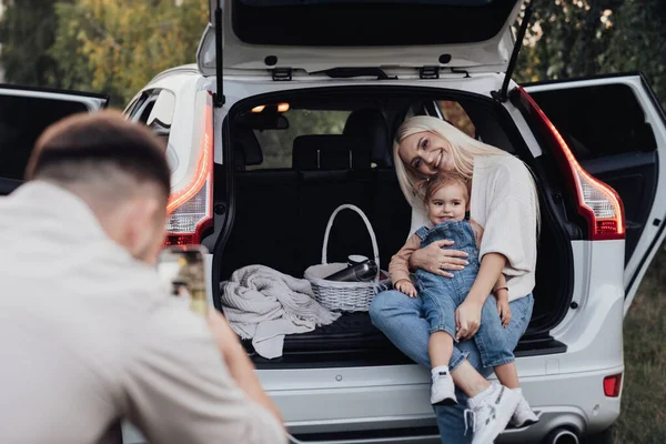 Mari Photographier sa femme et sa fille tout-petit qui sont assis dans le coffre ouvert d'une voiture SUV, vacances en voyage en famille — Photo