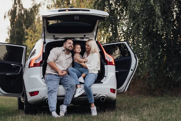 Familia joven sentada dentro del baúl abierto del coche de SUV, padres felices con su pequeña hija disfrutando de un viaje por carretera — Foto de Stock