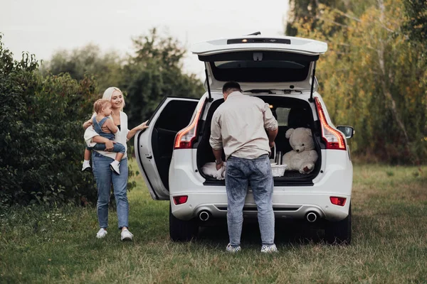 Dos padres con su pequeño niño preparándose para el picnic al aire libre, familia joven disfrutando de un viaje por carretera en el automóvil todoterreno —  Fotos de Stock