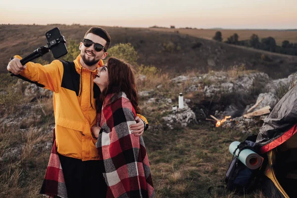 Junges Reisepaar macht Selfie auf dem Hügel vor Lagerfeuer und Zelt am Abend — Stockfoto