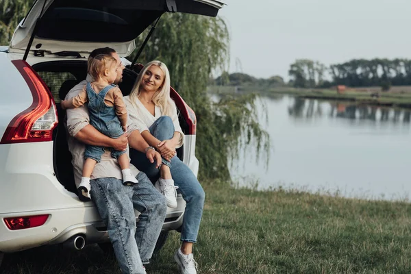 Jeunes parents avec une petite fille assis dans le coffre ouvert de la voiture, Happy Family profiter du voyage sur leur voiture SUV — Photo