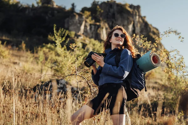 Porträt einer jungen Reisenden mit Sonnenbrille, Digitalkamera in der Hand und lächelndem Blick in die Ferne: Reiseleiterin genießt ihre beste Solo-Wanderung — Stockfoto