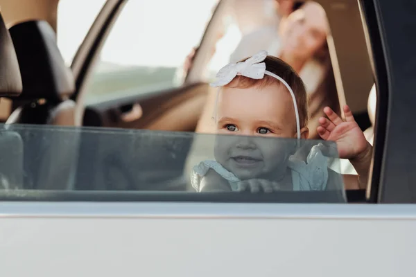 Niña caucásica sentada dentro del coche y agitando la mano imitando Hola a través de la ventana — Foto de Stock