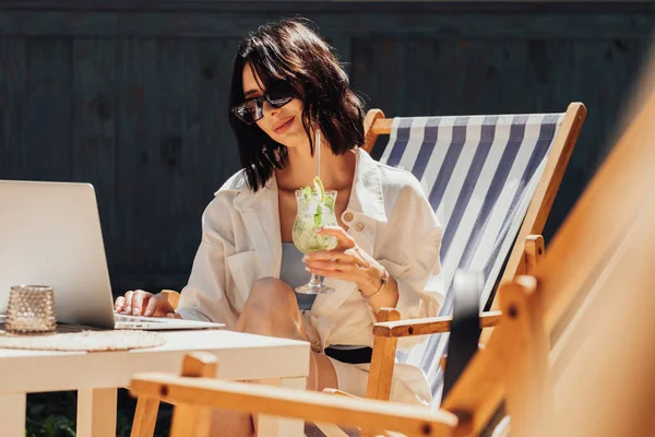 Sunglass Working on Laptop and Drinking Cocktail, Setting on the Terrace of the Restaurant, Freelancer at Work — 스톡 사진