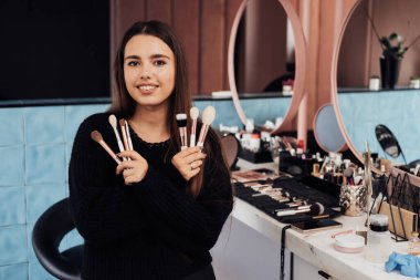 İş Yeri 'nde Katlanmış Kollu Genç Bir Kadın Makyaj Sanatçısı' nın Portresi, El Fırçaları ile Güzellik Salonunda Beyaz Kadın