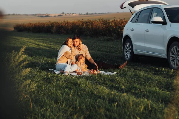 Glad ung familj njuter Road Trip på SUV bil, mamma pappa och deras dotter att ha picknick på helgen utomhus vid solnedgången — Stockfoto