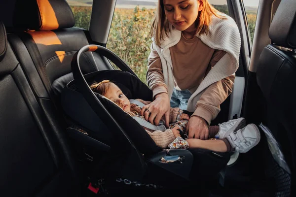 Young Mother Puts Her Baby Daughter in a Child Car Seat in the Car