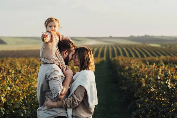 Felice giovane famiglia all'aperto, madre e padre con la loro figlia bambino al tramonto nel campo — Foto Stock