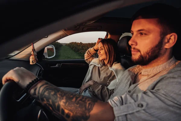 Dövmeli Kafkasyalı Adam ve Genç Kadın Sunset 'te arabada oturuyor, Hafta Sonu Yolculuğunun keyfini çıkaran bir çift — Stok fotoğraf