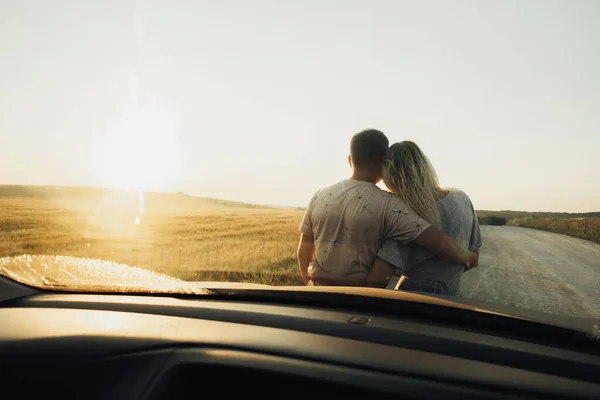 Voltar Ver através da janela do carro da frente em um casal jovem abraçando perto da capa, mulher e homem desfrutando de viagem ao pôr do sol — Fotografia de Stock