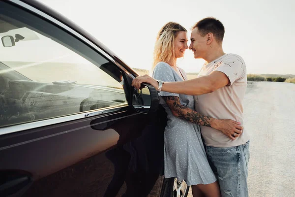Весела молода пара тримається біля автомобіля, татуйована жінка і Кавказький чоловік насолоджується дорожньою поїздкою на заході сонця — стокове фото