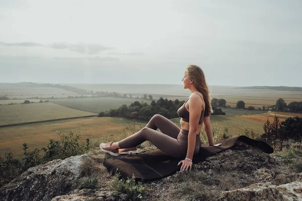 Bir Tepenin Üzerinde Oturan Genç Kadın, Güneşin batışında Panoramik Manzaranın tadını çıkaran Sportif Kız