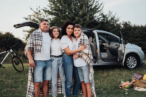 Quatro membros da família fazendo piquenique ao pôr do sol, uma mãe e um pai com duas crianças adolescentes desfrutando de viagem de fim de semana de carro — Fotografia de Stock