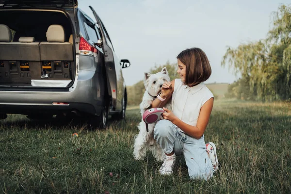 Menina adolescente brincando com West Highland White Terrier Dog no fundo do carro Minivan ao ar livre — Fotografia de Stock