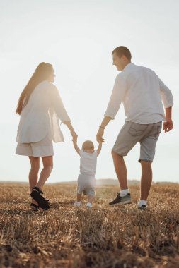 Anne ve babasının, çocuklarının ilk adımlarını atmasına yardım ederken, Sunset 'te Genç Aile Sahada Yürüyüşü