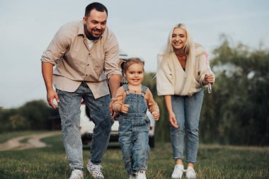 Mutlu genç aile dışarıda eğleniyor, küçük kız ailesinden kaçarak oynuyor.