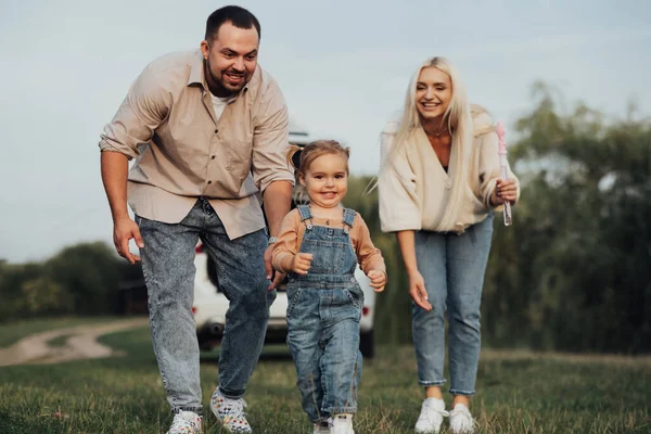 Mutlu genç aile dışarıda eğleniyor, küçük kız ailesinden kaçarak oynuyor.