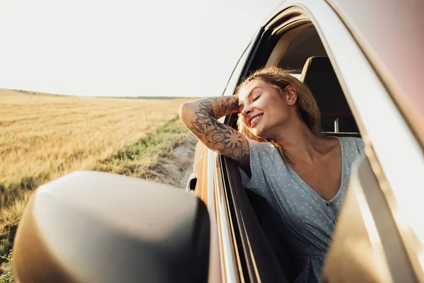 Happy Tattooed Girl Enjoying Road Trip, Young Woman Relaxing and Looking Out Car Window