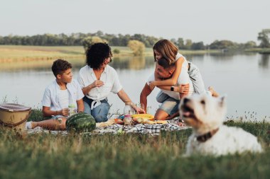 Mutlu Dört Üye Aile ve Köpek Sunset 'te piknik yapıyor Neşeli Anne ve Baba ve İki Genç Çocuk ve Evcil Hayvan Keyifli Hafta Sonu Göl kenarında