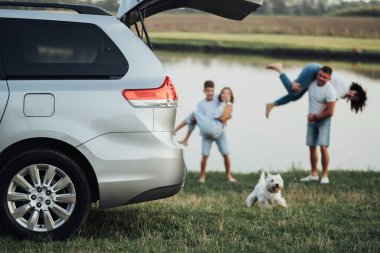TERNOPIL, Ukrayna - 12 Eylül 2021: Gri Toyota Sienna Açık Bagajlı ve Bulanık Mutlu Dört Üye Ailesi ile Nehir kenarında Evcil Köpek Eğleniyor