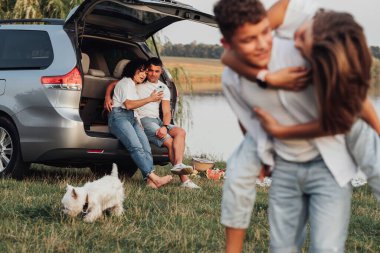 Çocuklar Lake, Four Members Family ve Pet Dog 'la hafta sonu pikniği yaparken Mutlu Anne ve Baba Minivan Car' ın bagajında oturuyor.