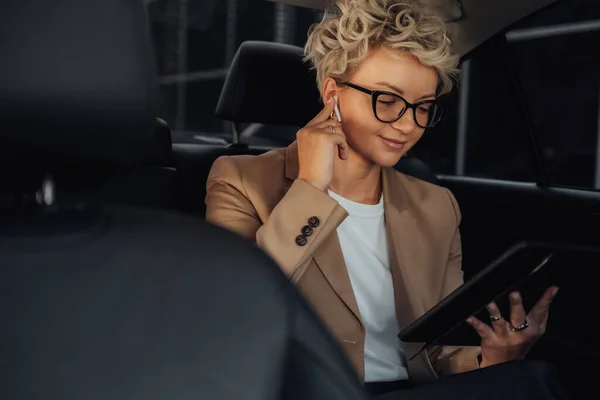 Business Woman Sitting on Back Seat of Luxury Car and Having Video Conversation Through Tablet