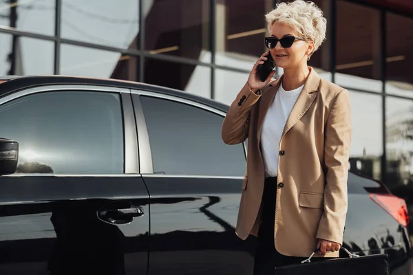 Elegant Business Woman with Briefcase in Hand Talking on Phone Near the Luxury Car