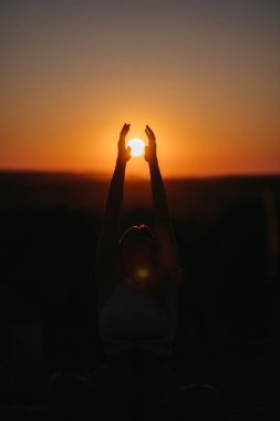 Silhouette of Unrecognisable Woman Catching the Sun That Going Under Horizon by Hands at Sunset