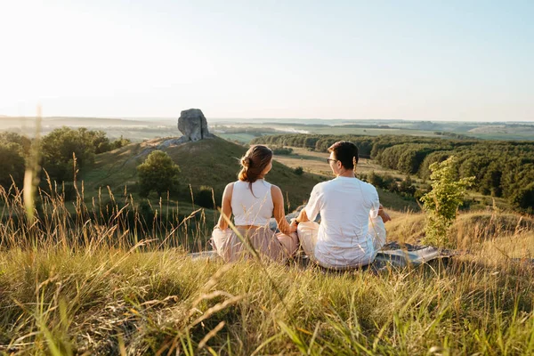 Man and Woman Practicing Yoga and Meditation Outdoors at Sunset with Scenic Landscape and Nature Miracle Giant Stone on Background