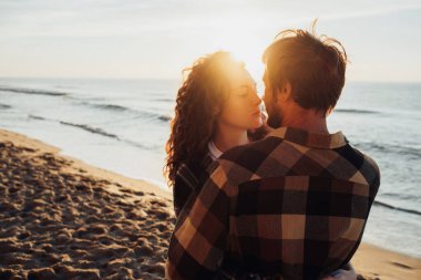Young woman and man hugging together and come for a kiss against the background of sea and the suns rays at dawn